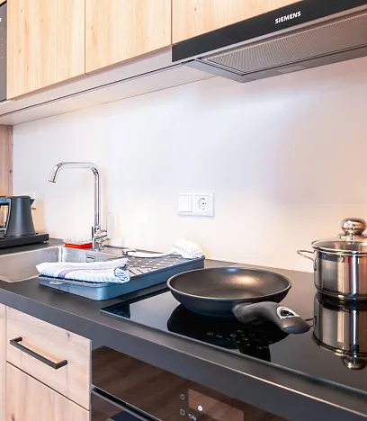 Moderne Küchenzeile mit Holzoberflächen, schwarzer Arbeitsplatte, Induktionskochfeld, Edelstahlkochtopf, Bratpfanne, Spüle und Kaffeemaschine.